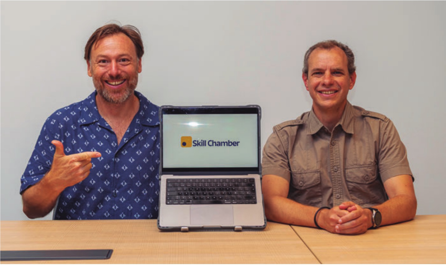 Adam Giles and Ernesto Buttó with a laptop displaying the Skill Chamber logo